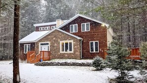 Een chalet met twee verdiepingen, een stenen gevel en een houten uitbouw, omringd door een besneeuwd bos.