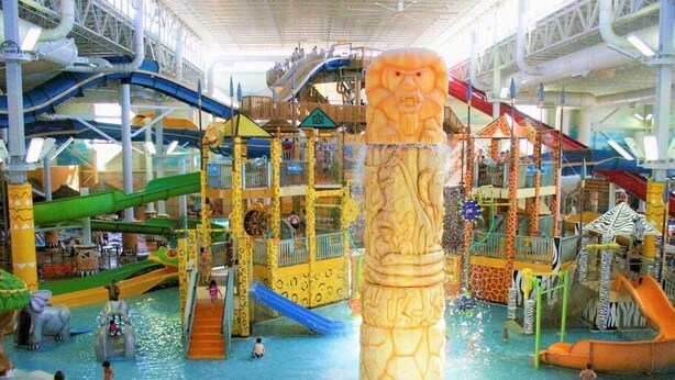 Een overdekt waterpark met glijbanen, een grote centrale waterzuil en diverse speelconstructies.