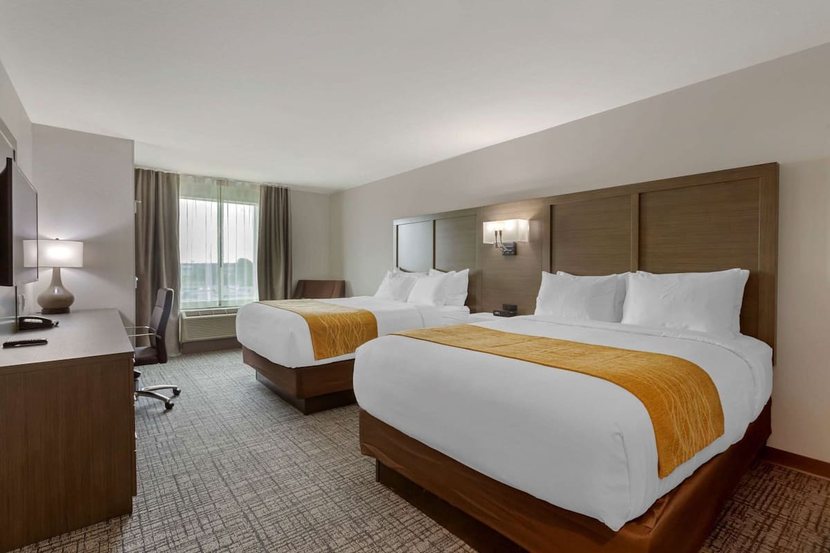 A hotel room with two beds, a desk, a chair, a lamp, and a window with curtains.
