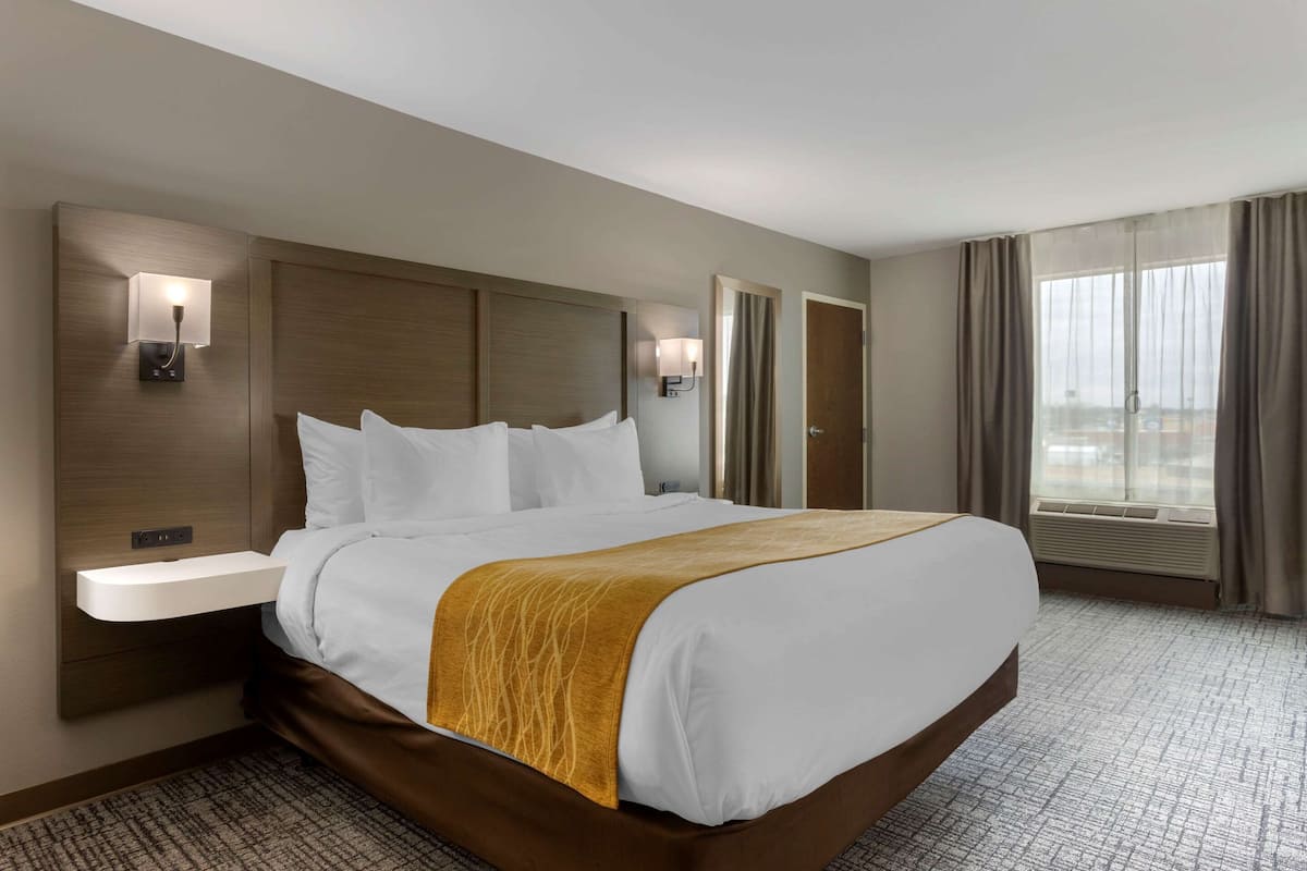 A hotel room with a large bed, bedside tables, a headboard, and a window with curtains.