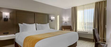 Habitación de hotel con una cama grande, mesitas de noche, un escritorio con silla, una ventana con cortinas y lámparas de pared.