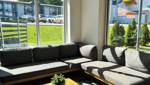 Una sala de estar moderna con un sofá modular, una mesa de centro de madera con una planta y ventanas amplias que ofrecen vistas a la calle y al entorno verde.
