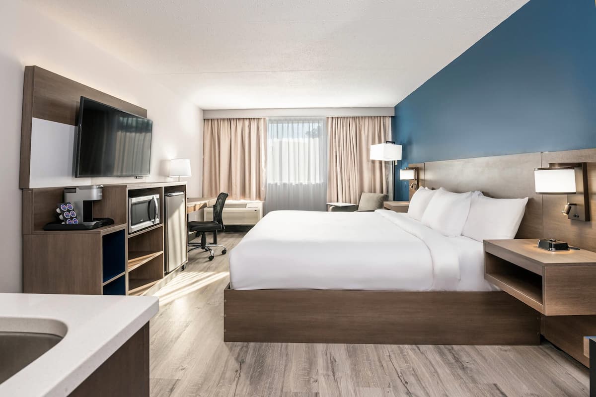 Una habitación de hotel moderna con una cama grande, un televisor de pantalla plana, un escritorio con lámpara y una kitchenette.