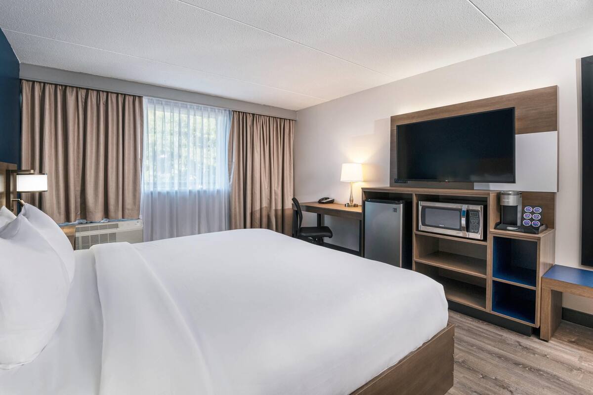 Una habitación de hotel con una cama grande, un escritorio con computadora, televisor, microondas y cafetera.