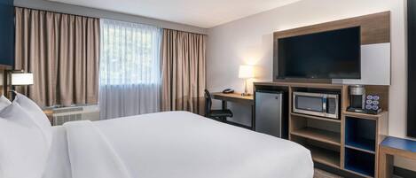 A hotel room with a large bed, a desk with a computer, a television, a microwave, and a coffee maker.