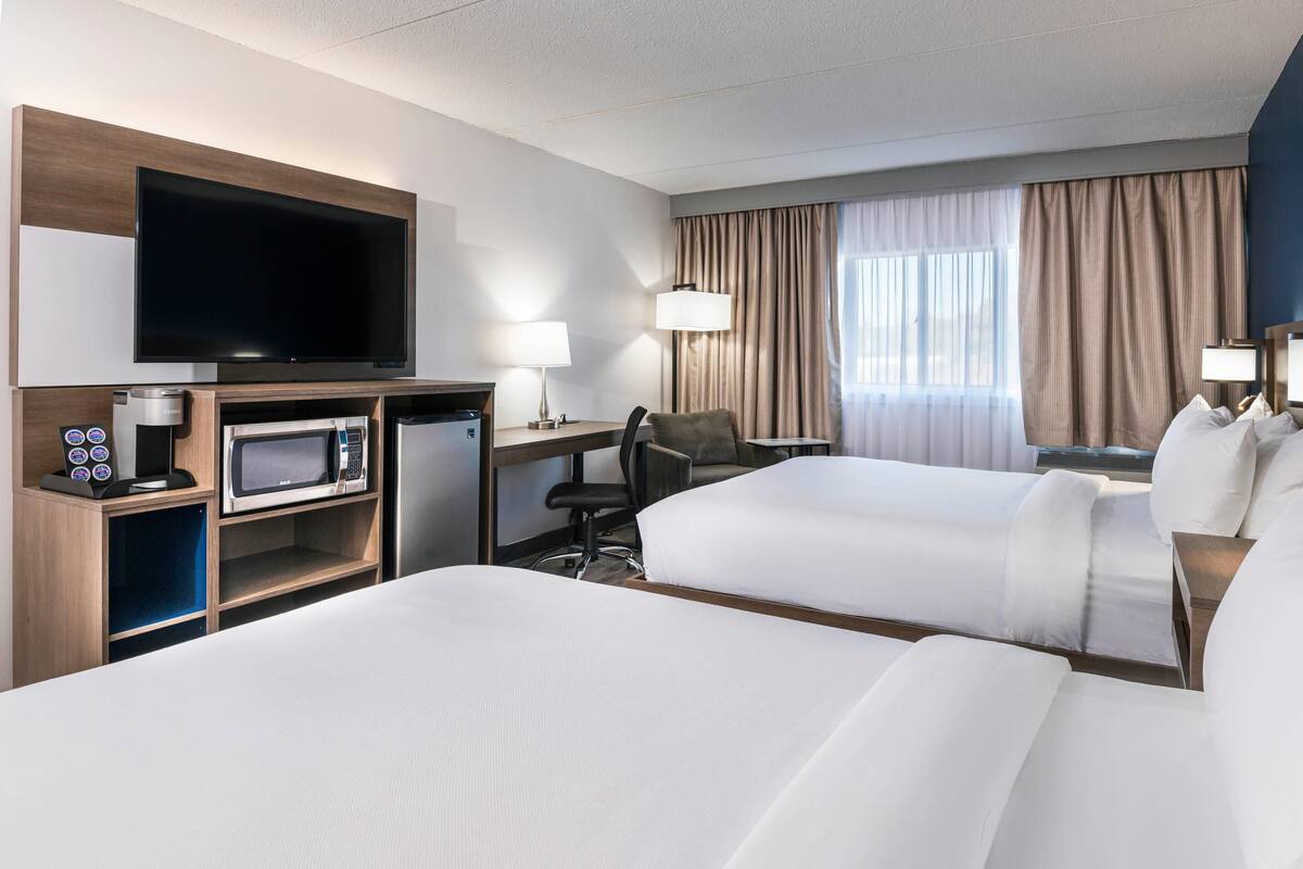 Habitación de hotel con dos camas, un televisor de pantalla plana, microondas, cafetera, escritorio y una silla.