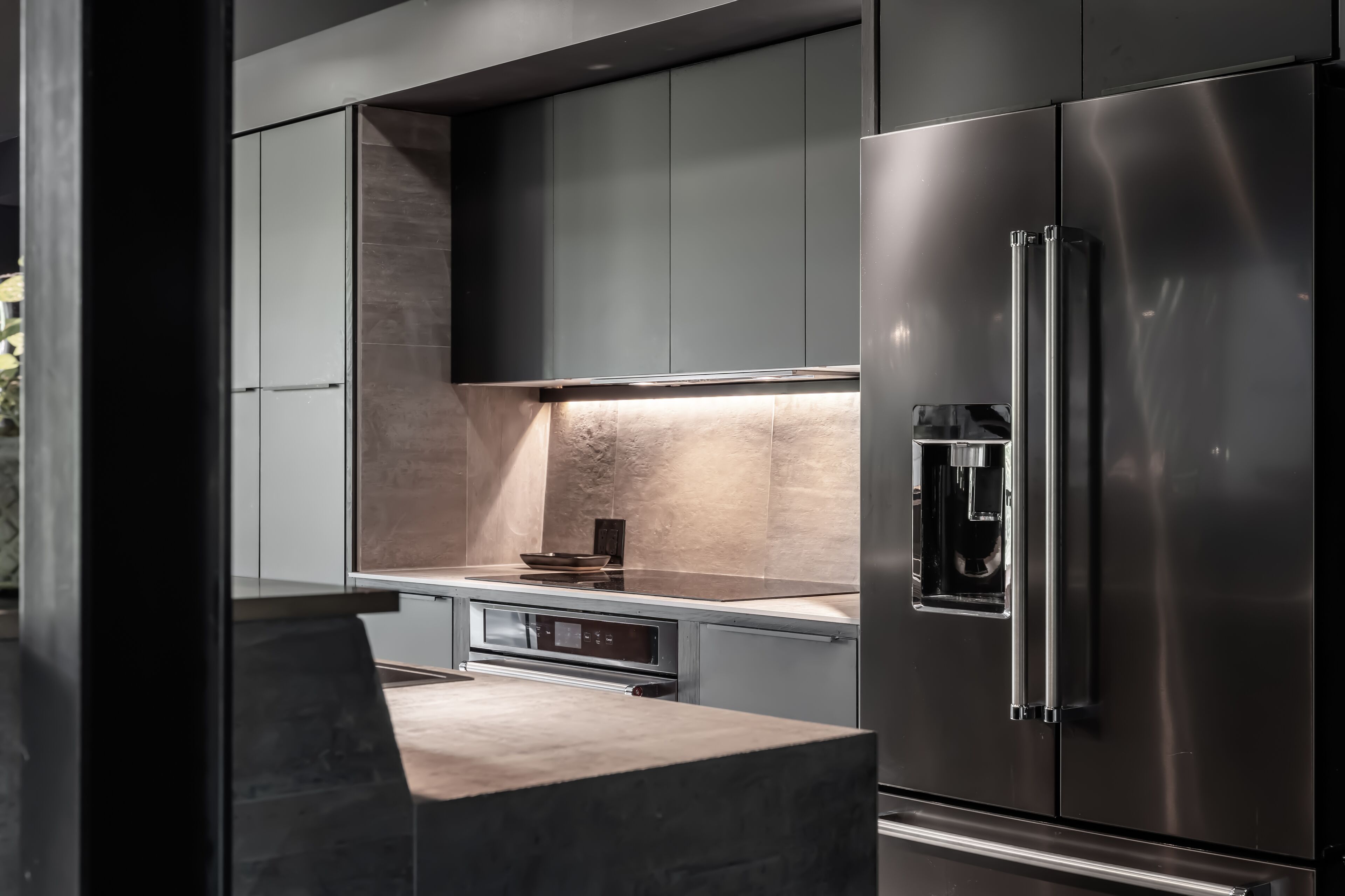 A modern kitchen with dark cabinetry, a stainless steel refrigerator, and a built-in oven.
