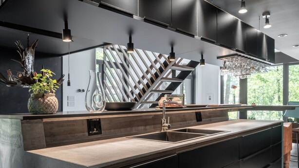 Una cocina moderna con una isla central, muebles negros y luminarias colgantes.