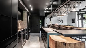 Una cocina moderna con armarios oscuros, una isla de madera y cristalería colgante.