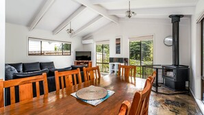 A spacious living area with a wooden dining table, a black leather sofa, and a black fireplace. - WAVELENGTH - Free Wifi and Pet Friendly (outside only) (Inverloch)