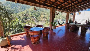 A covered patio with a table and chairs, a hammock, and a view of a mountainous landscape.