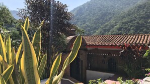 A traditional building with a tiled roof, surrounded by lush greenery and a mountainous backdrop.