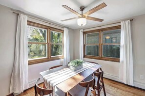 A dining area with a wooden table, white curtains, and a ceiling fan. - Waterfront Haven! Kayaks Included w/Hot Tub (Green Bay)