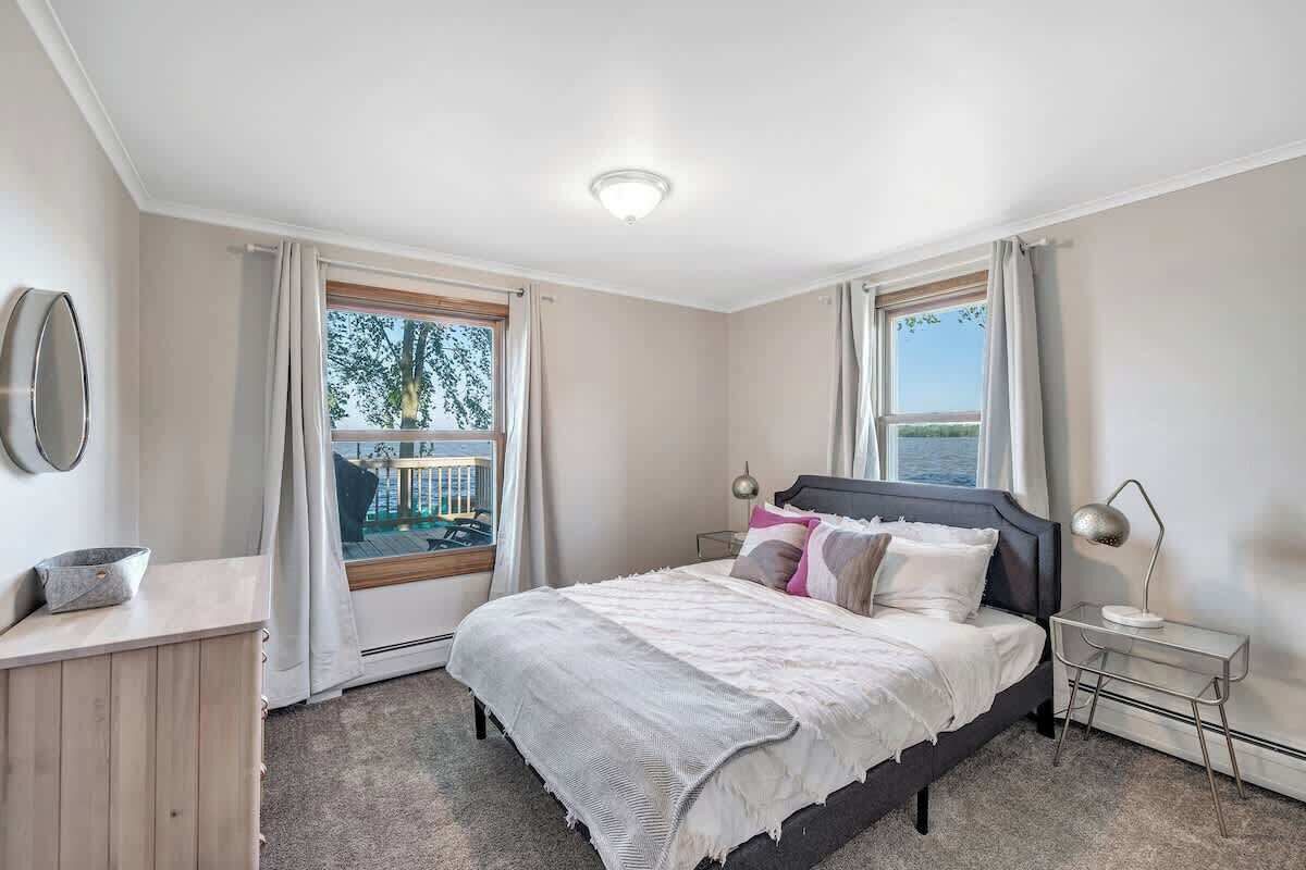 Een slaapkamer met een bed, nachtkastje, lamp en uitzicht op het natuurlijke landschap door een raam.
