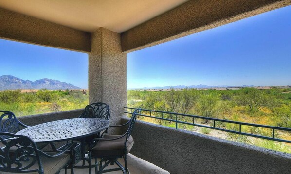 A balcony with a table and chairs, offering a view of a desert landscape with mountains.