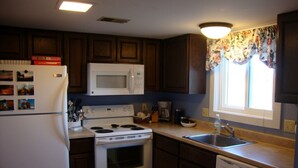 A kitchen with dark wooden cabinets, a white refrigerator, a microwave, a stove, a dishwasher, and a window with floral curtains. - 2King Master Suites, Walk to golf, Outside heated pool (Cedar)