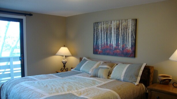 A bedroom with a large bed, a nightstand, a lamp, and a painting on the wall. - 2King Master Suites, Walk to golf, Outside heated pool (Cedar)