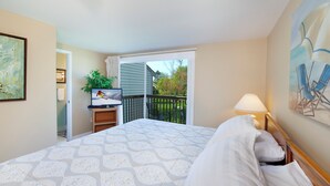 A bedroom with a bed, a TV on a stand, a balcony with chairs, and a painting on the wall. - 2 King Master Suites, Outside heated pool, Close to Dunes (Cedar)