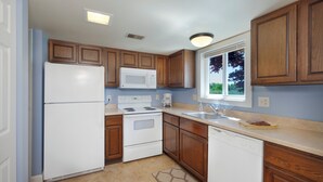 A kitchen with wooden cabinets, a white refrigerator, a microwave, an oven, a dishwasher, and a window with a view of trees. - 2 King Master Suites, Outside heated pool, Close to Dunes (Cedar)