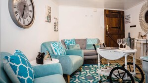 A cozy living room with a vintage clock, a wooden door, and a small table with glasses and a bottle. - Casa a Boleriña 1 (Poio)