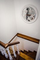 Una escalera con paredes blancas, barandilla de madera y un espejo decorativo con diseños ornamentales.