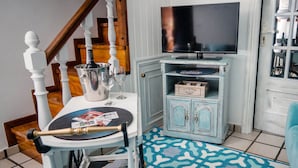 A dining area with a wooden chair, a table with a wine bottle and glasses, a television on a cabinet, and a patterned rug. - Casa a Boleriña 1 (Poio)