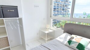 A bedroom with a bed, a desk, and a wardrobe. There is a window with a view of buildings and plants. - Skol 645 - Exclusive 3-Bedroom Apartment with Sea Views (Marbella)