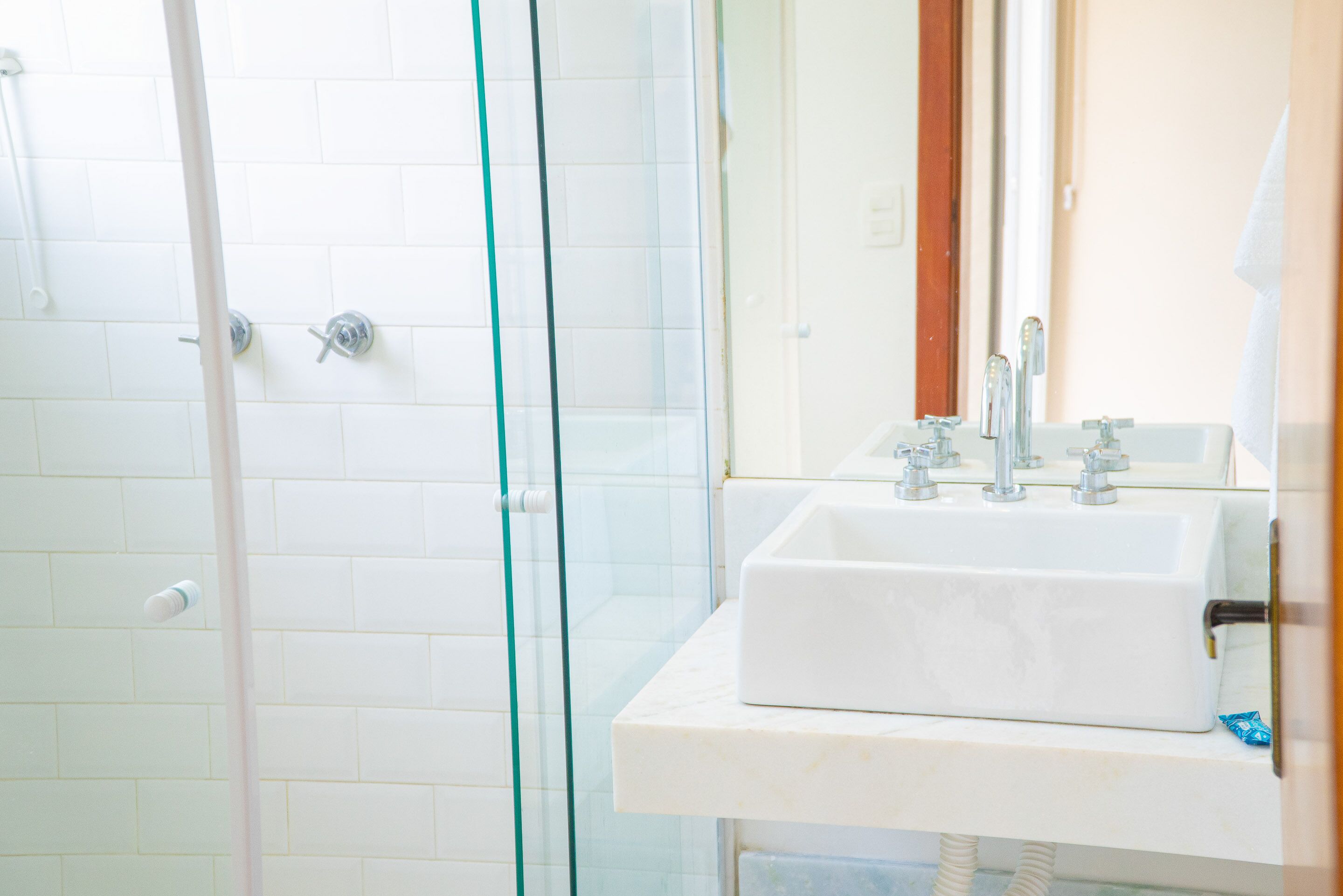 A bathroom with a glass shower enclosure, a white sink with a mirror, and a white tiled wall.