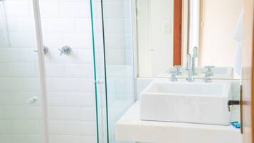 A bathroom with a glass shower enclosure, a white sink with a mirror, and a white tiled wall.