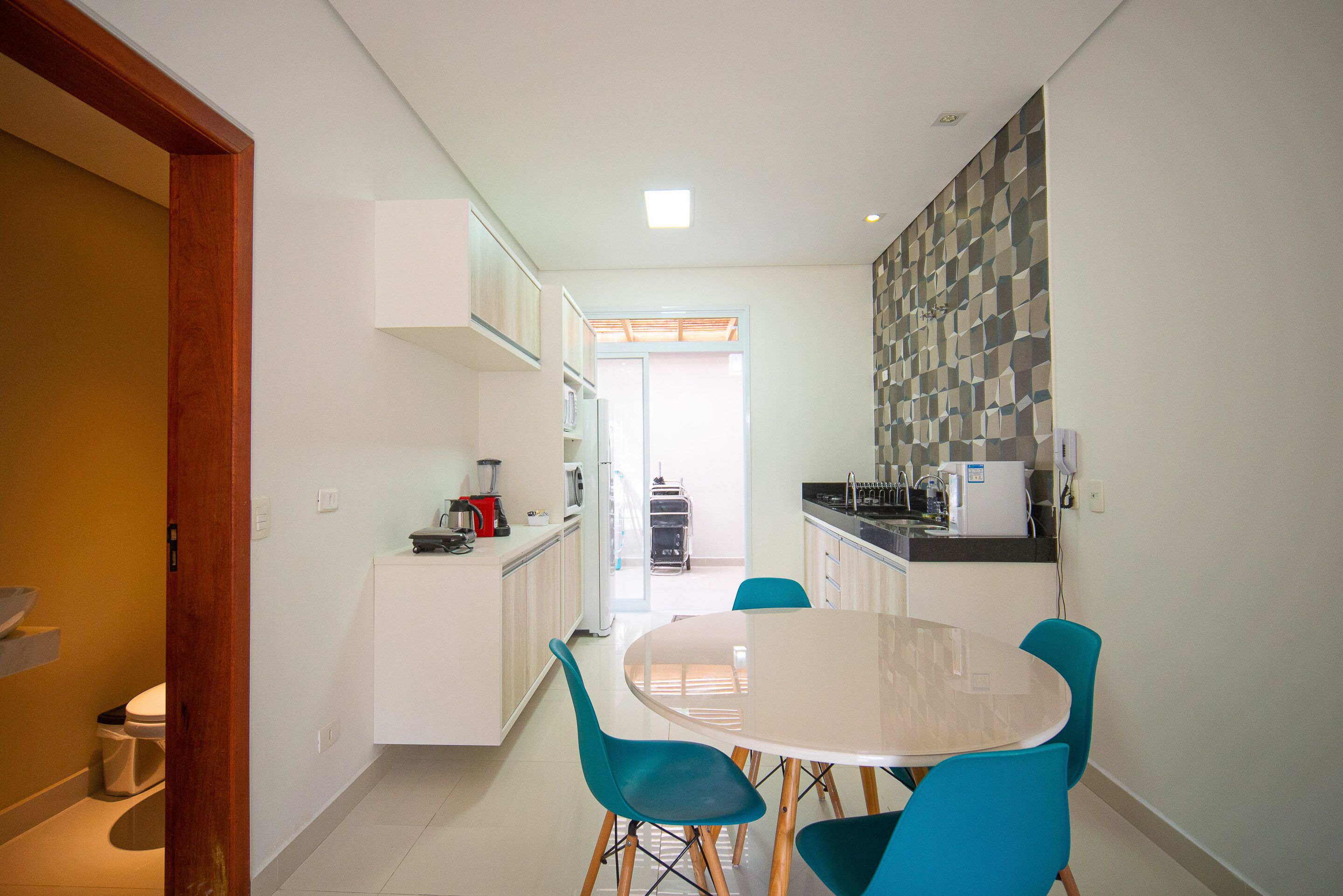 A modern kitchen with white cabinets, a dining table with four chairs, and a view into the adjacent living area.