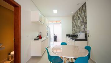 A modern kitchen with white cabinets, a dining table with four chairs, and a view into the adjacent living area.