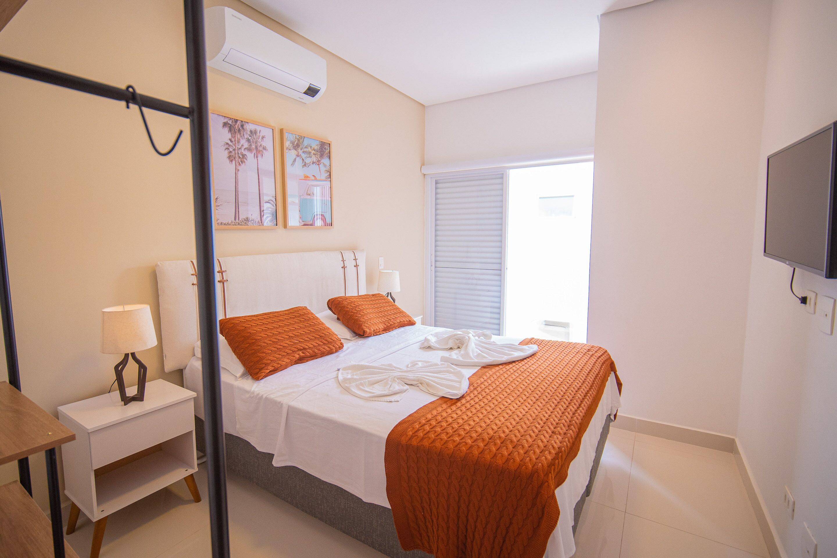 A hotel room with a bed, a nightstand, a lamp, a TV, and a window with blinds.