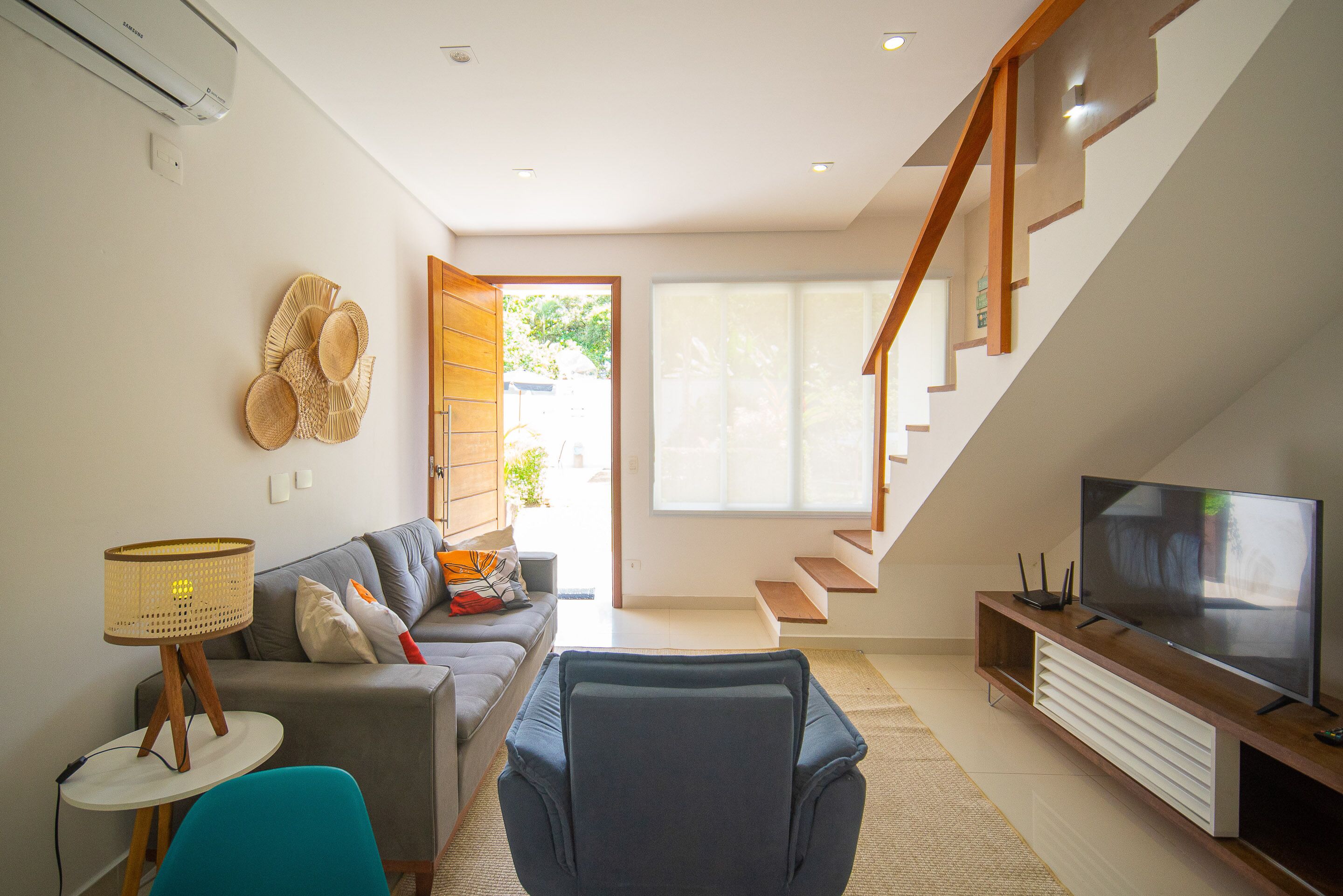 Un salon moderne avec un canapé, un fauteuil bleu, un téléviseur et un escalier menant à l’étage supérieur.
