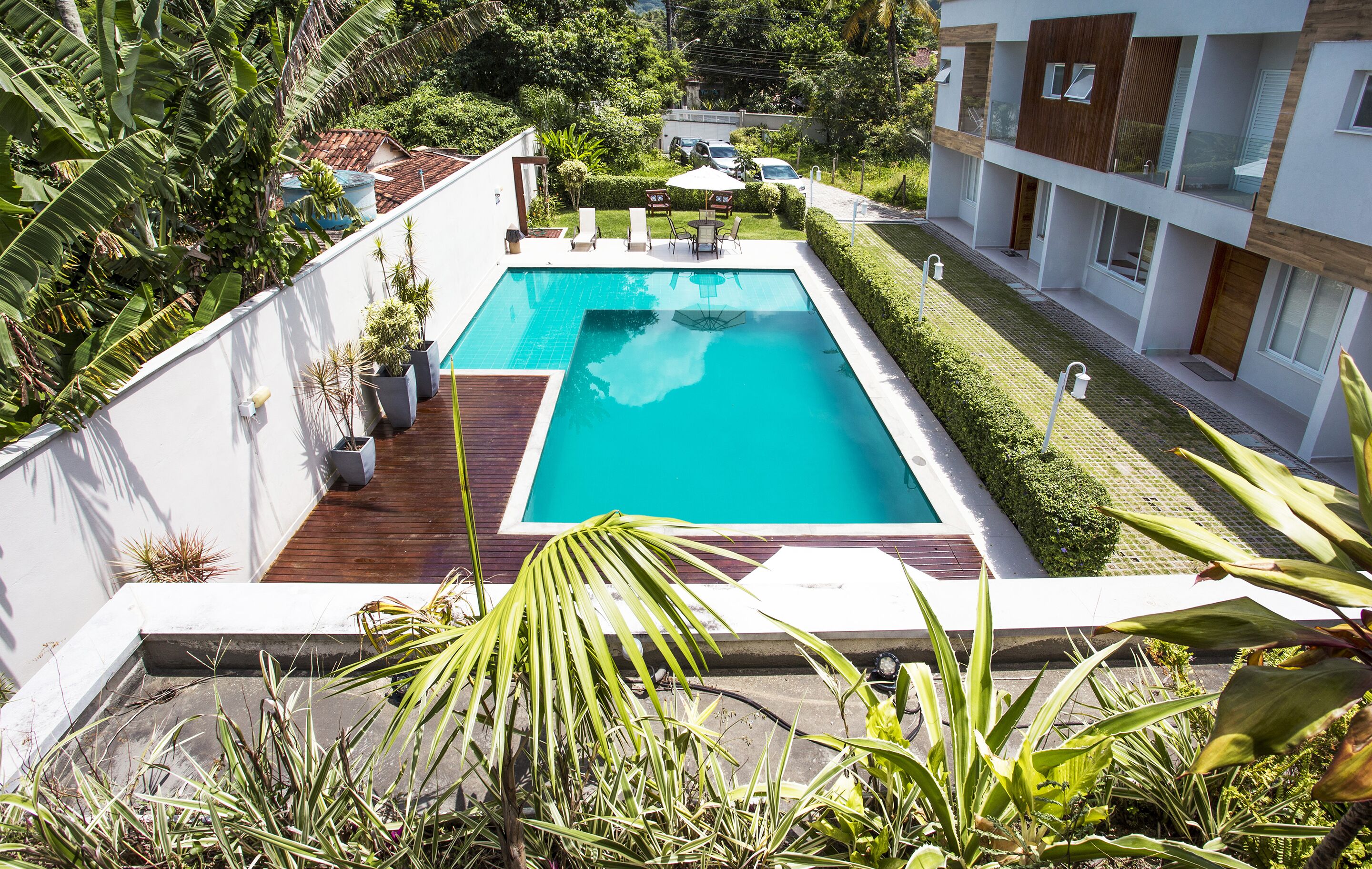A modern pool area with a rectangular pool, surrounded by potted plants and a wooden deck.
