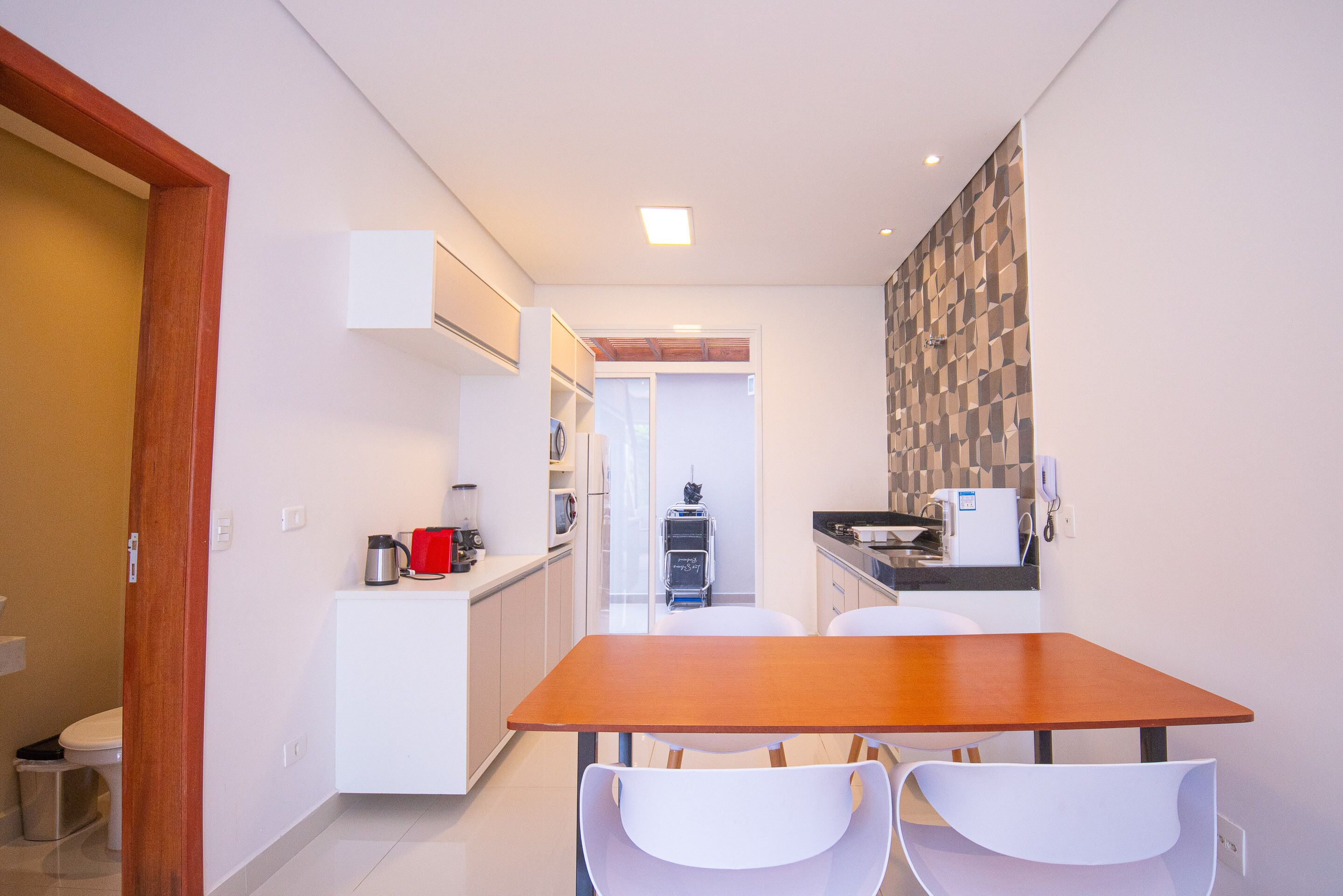 A compact kitchen with a wooden table and white chairs, a microwave, and a coffee maker.