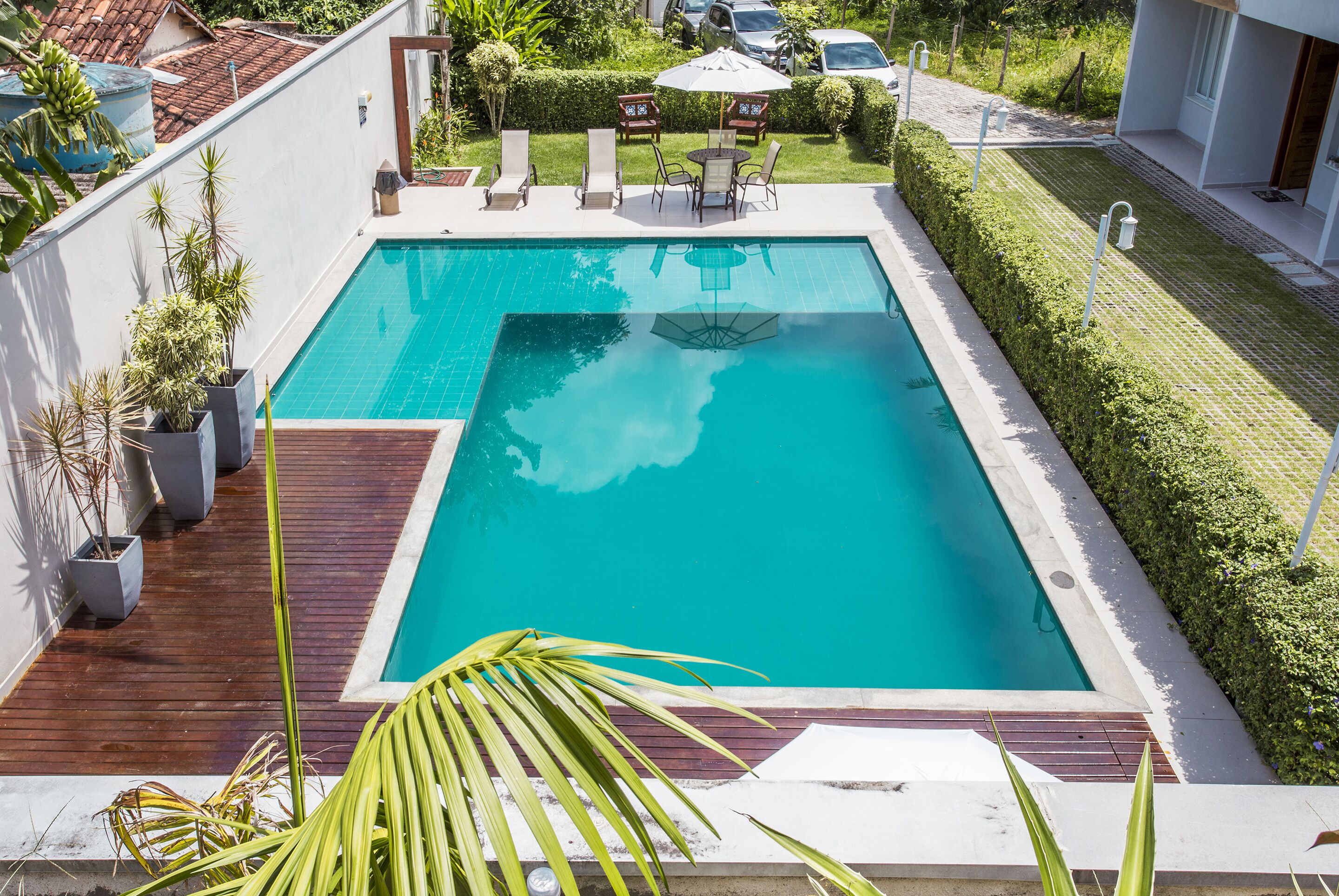 Piscina retangular com deck de madeira e plantas em vasos.