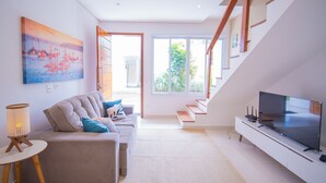 A modern living room with a sofa, a TV, and a staircase leading to an outdoor area. - Residencial Las Salinas (São Sebastião)