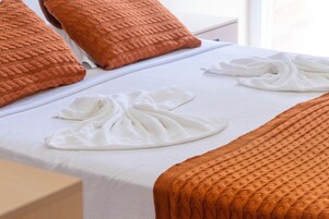 Una cama bien hecha con sábanas blancas y dos almohadas naranjas.