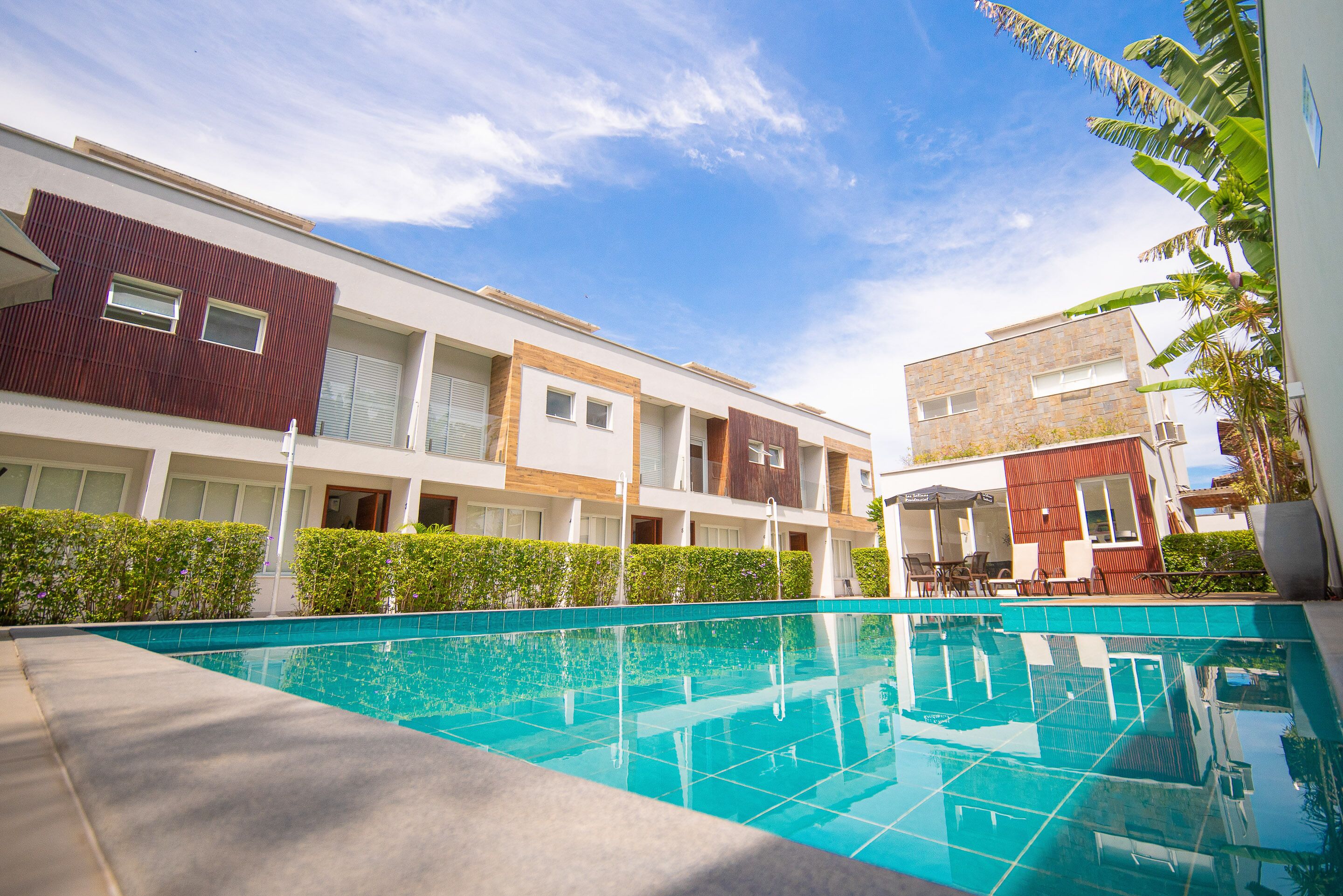 A modern hotel with a swimming pool, multiple balconies, and a clear blue sky.