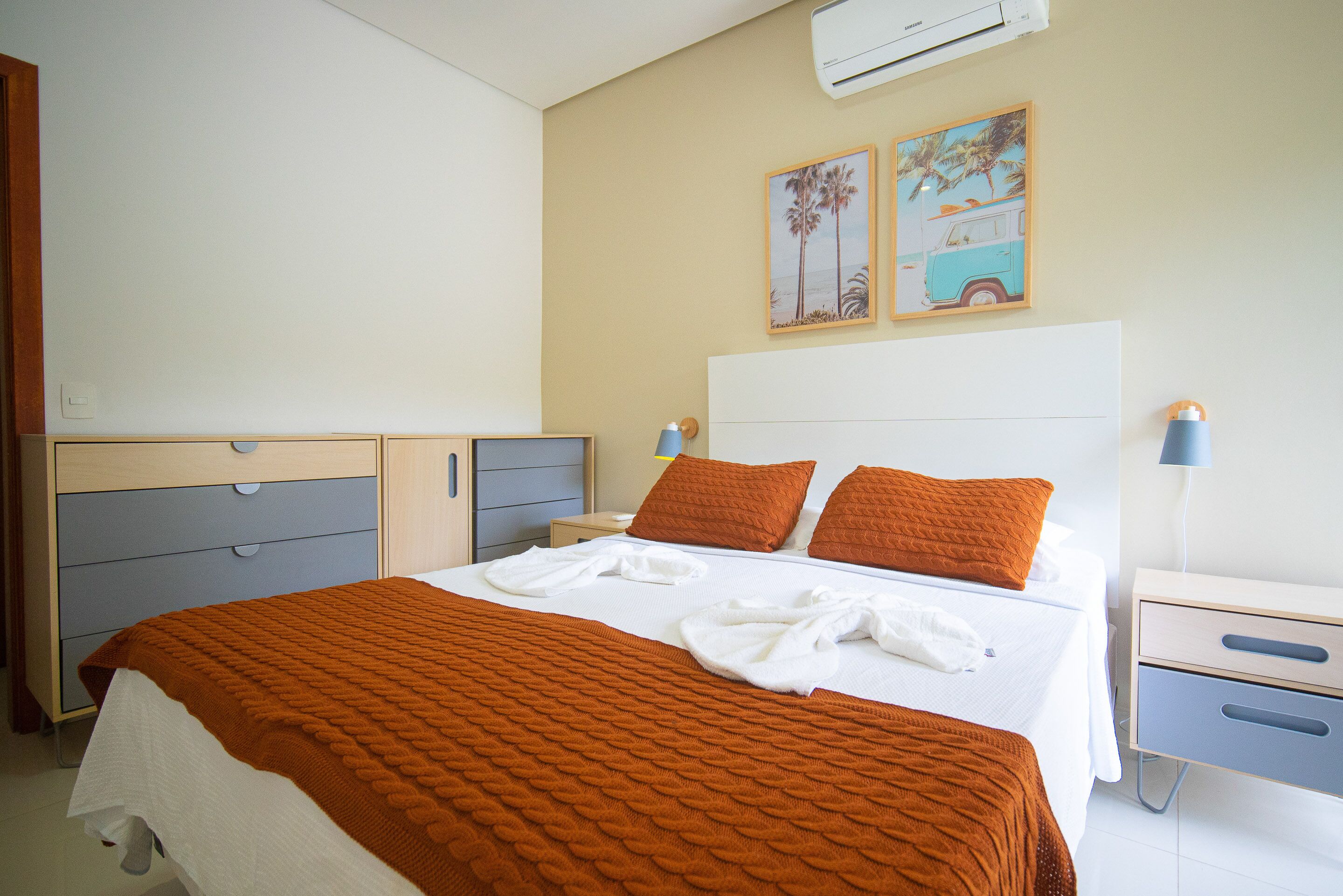 A hotel room with a large bed, two pillows, a bedside table with a lamp, and a nightstand.