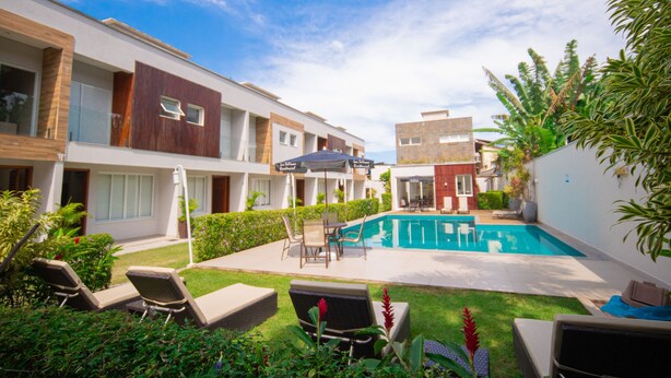 A modern hotel with a swimming pool, outdoor seating, and lush greenery. - Residencial Las Salinas (São Sebastião)