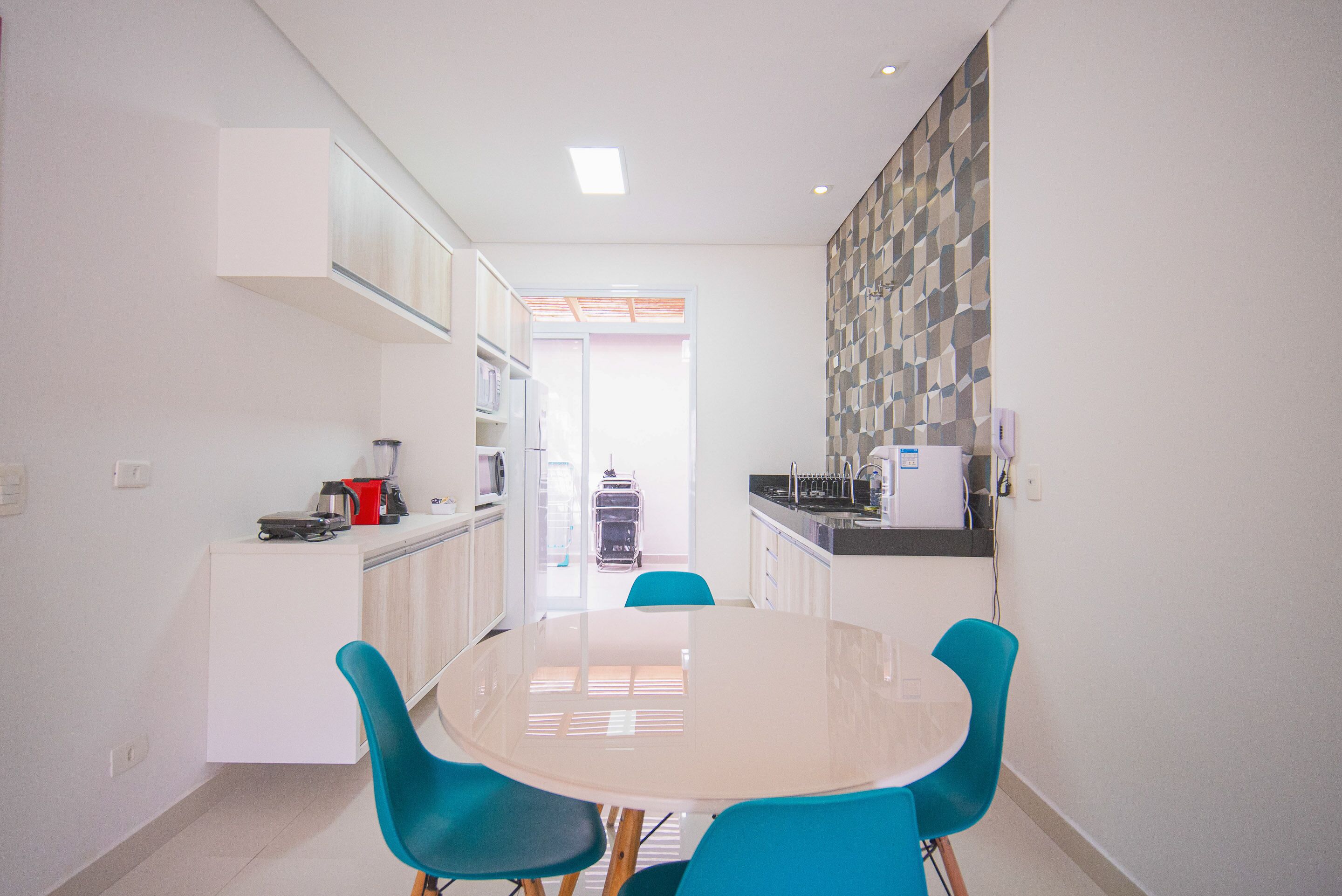 A modern kitchen with white cabinets, a microwave, and a coffee maker. There is a dining table with four blue chairs.