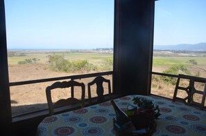A room with a table and chairs, a window with a view of a field and mountains, and a bottle on the table. - Lighthouse Ranch with Expansive Ocean and Pasture Views (Point Arena)