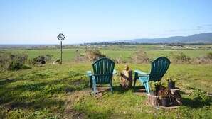 Dos sillas Adirondack verdes en un campo de hierba con un molino de viento al fondo.