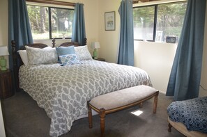 A bedroom with a large bed, a bench, two bedside tables, and a window with curtains. - Lighthouse Ranch with Expansive Ocean and Pasture Views (Point Arena)