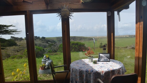 Un invernadero con una mesa dispuesta para dos, una silla y vistas al campo.