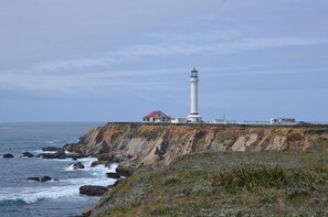 A lighthouse on a cliff with a red-roofed building nearby. - Lighthouse Ranch with Expansive Ocean and Pasture Views (Point Arena)
