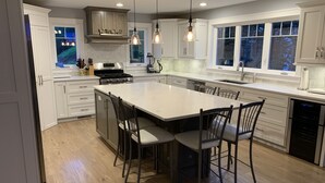 A modern kitchen with white cabinetry, a large island with bar stools, a built-in oven, and pendant lighting. - Waterview 5 bedroom home.  Sleeps 10 (Cornwall)