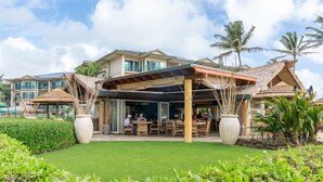 Un resort con un área de estar al aire libre techada, palmeras y un césped bien cuidado.