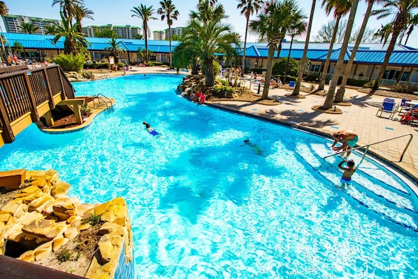 A swimming pool with clear blue water, surrounded by palm trees and lounge chairs.